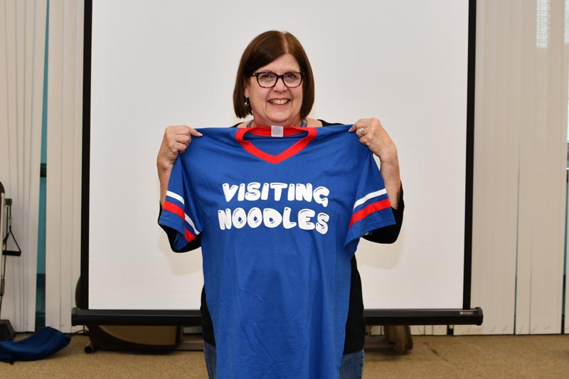 Janice holds up a Visiting Noodles shirt that was given to her for her 49th anniversary at VNA. 