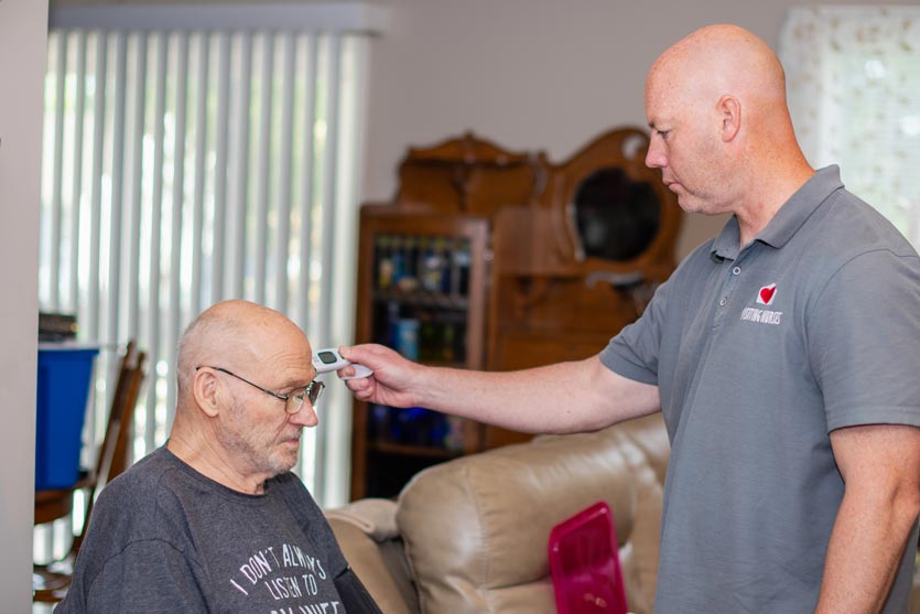 Chad, an OTA with Visiting Nurses Home Health, checks Dave Aikins' temperature while recording his vitals on a visit. 
